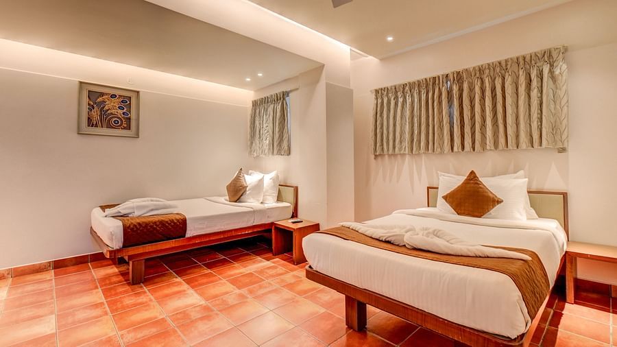 A spacious room at Harigovinda's JNStay with two neatly made beds and window covered by curtains