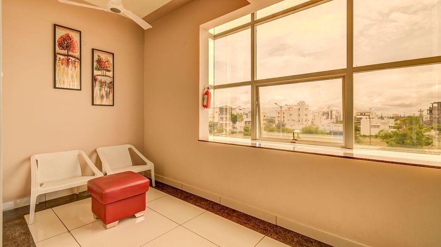 Two chairs placed before a small cushioned table beside a large glass window at Harigovinda's JNStay