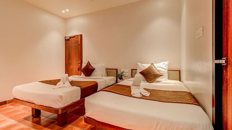 Two neatly made beds placed side by side, with a door to the side at Harigovinda's JNStay