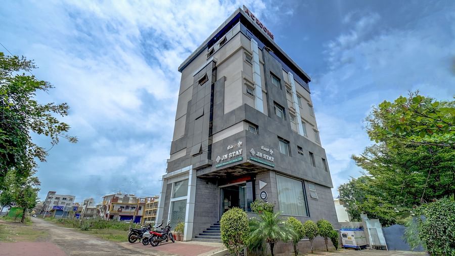 Diagonal view of Harigovinda's JNStay exterior with trees to the side against a cloudy sky