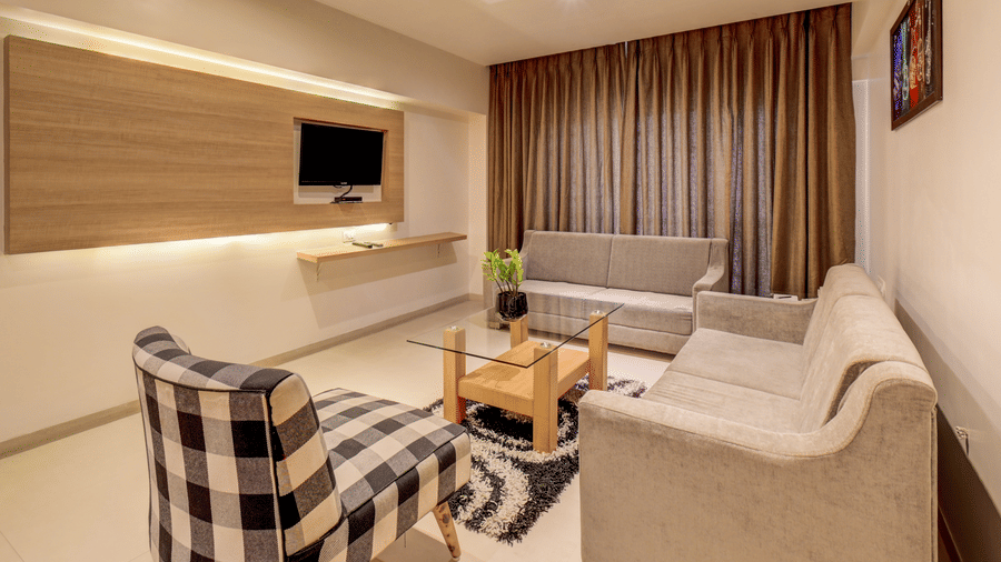 Sofas and an armchair are positioned around a central coffee table in front of a wall structure. This arrangement highlights the sitting room area of a Suite Room at The SSK Solitaire Hotel & Banquets, Mumbai Naka - Nashik.