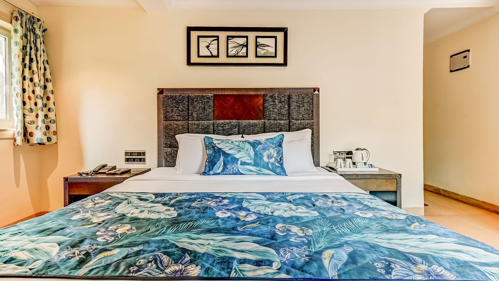 Deluxe room with a private balcony featuring a large bed, flanked by wooden bedside tables, and a photo frame mounted above the headboard