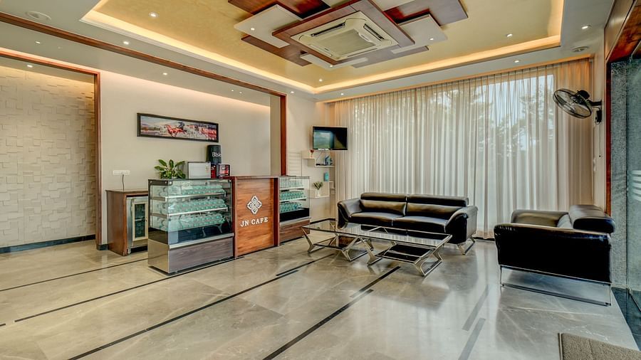 A diagonal view of the reception area at Harigovinda's JNStay, with a desk to the side and a cushioned sofa with a table in front