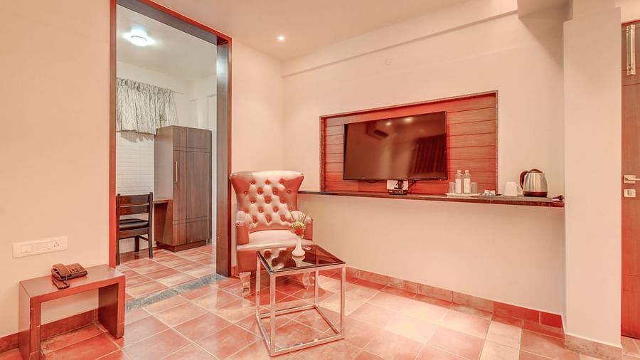 A room at Harigovinda's JNStay with a wall-mounted TV, a chair next to the doorway, and a bedside table