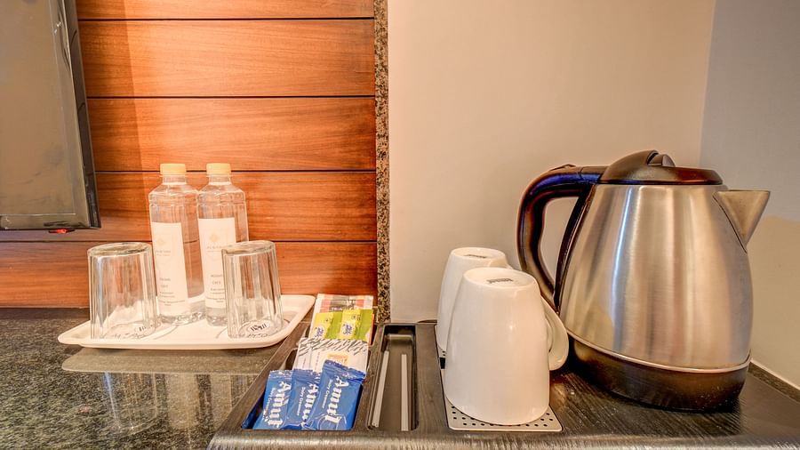 Two trays at Harigovinda's JNStay: one with glasses and water bottles, and the other with cups, snacks, and a kettle