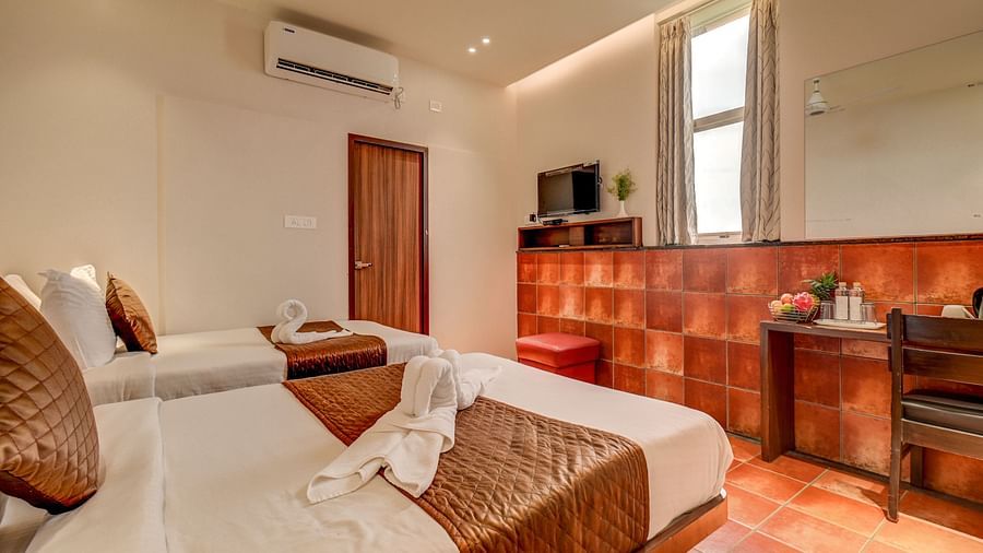 A spacious room at Harigovinda's JNStay with two beds, a wall-mounted TV, and a wooden desk to the side