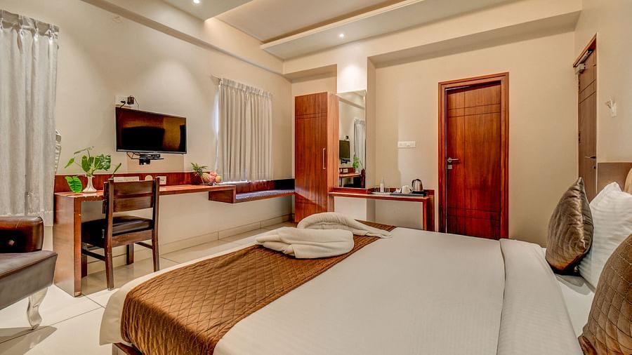 A view of a spacious bed, wall-mounted TV, desk below it, and a chair beside the side table at Harigovinda's JNStay