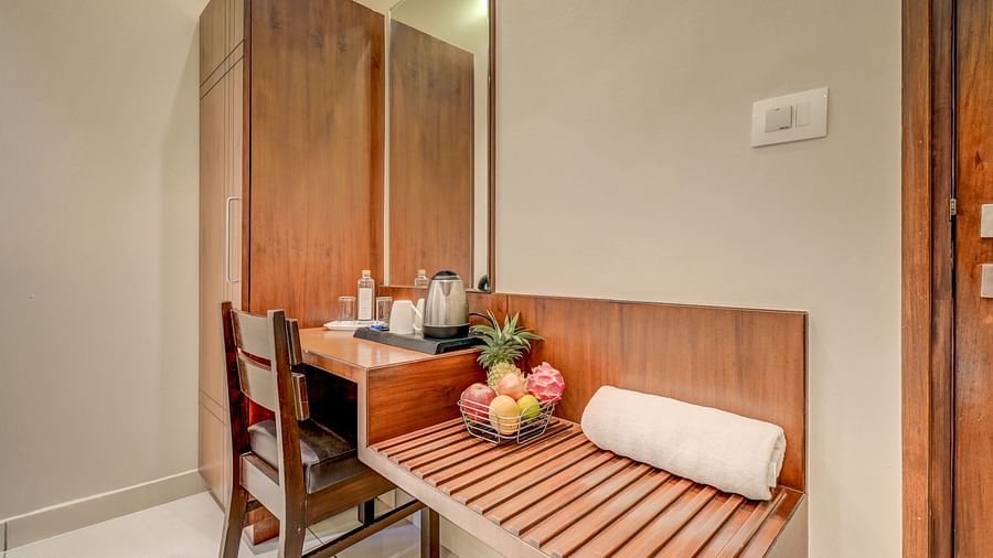 A wooden wardrobe with a wooden table and chair adjusted to it, and a towel and fruit basket placed on the table at Harigovinda's JNStay
