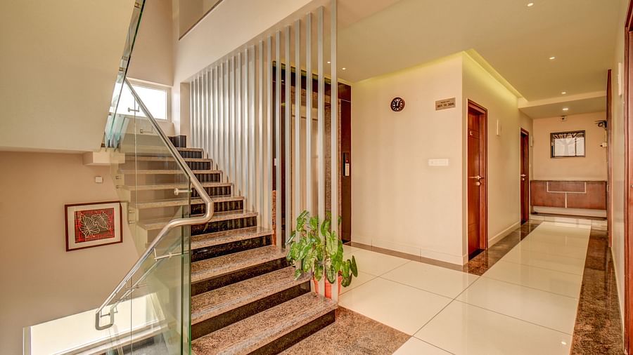 Stairs with glass panels on one side and a corridor leading to rooms on the other at Harigovinda's JNStay
