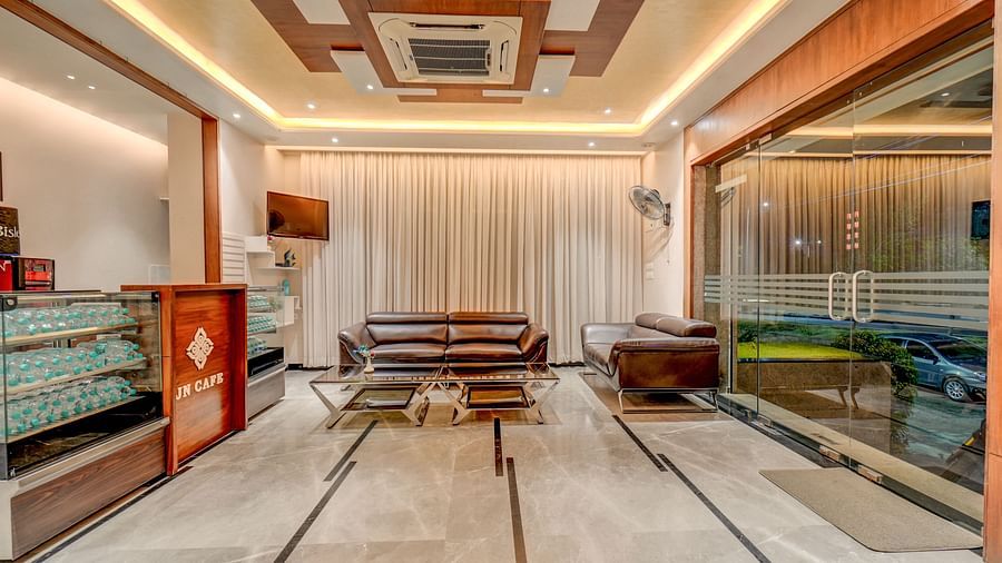 The reception area at Harigovinda's JNStay, featuring a desk to the side, a cushioned sofa with a table in front, and a glass-panelled wall beside the sofa