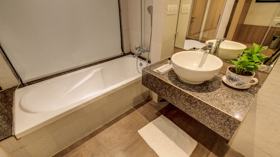 A bathtub stands installed against a wall next to a stone vanity unit with a wash basin. This view captures the bathroom amenities provided in a Suite Room at The SSK Solitaire Hotel & Banquets, Mumbai Naka - Nashik.