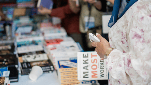 A person is holding their mobile phone while standing in front of a display of books and magazines.