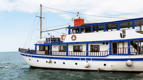 A white and blue ferry boat sailing on the water with passengers visible on the deck.