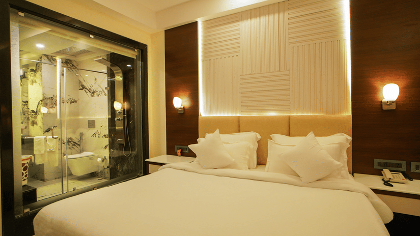 A plush bed with white bedding rests next to a modern glass-walled bathroom inside a bedroom at Shanti Seaview Resort & Spa.