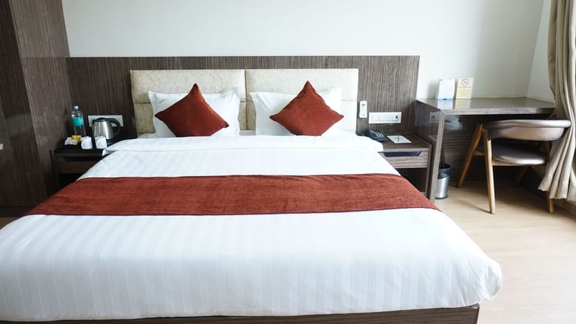 Elegant well lit bedroom with a king bed, a side table and a chair at the Aanandam Hotel Resort.