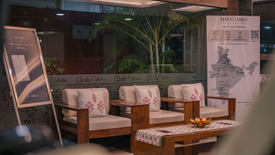 The lobby seating area with chairs, table and flower vase on the table, view of the trees outside the glass window, and a large window at Clarks Collection, Vadodara.