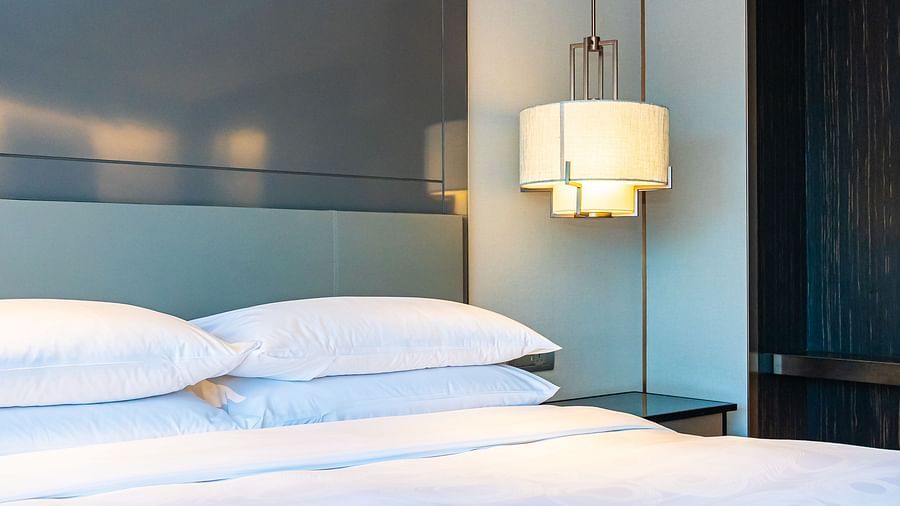 A cosy room featuring a neatly made double bed with white linens, a headboard, and a warm bedside lamp.