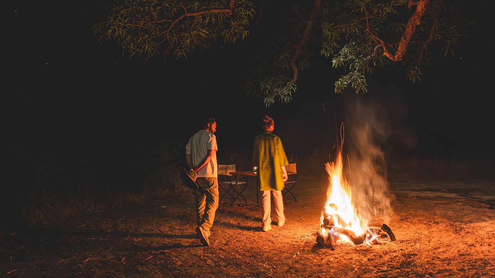 Two people walking around a bonfire at Trees N Tigers, Tadoba.