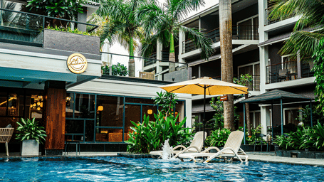 The swimming pool featuring wooden seating, umbrellas, and landscaped greenery, beside the Sundowner Cafe | Hotel Sonar Bangla, Tarapith