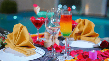Poolside table set with layered cocktails, wine glasses, gold napkin fans, plates and rose petal decorations at Polo Hotel, Agartala.