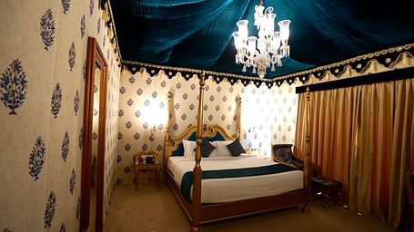 Image of a room with a bed, a mirror on the side and a chandelier hanging from the ceiling.