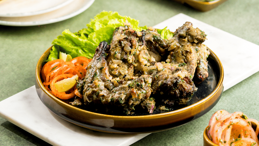 A close up of a kebab with sautéed onions on top of it, pickled onions and lettuce on the side, served at Zaika in Gemini Continental.