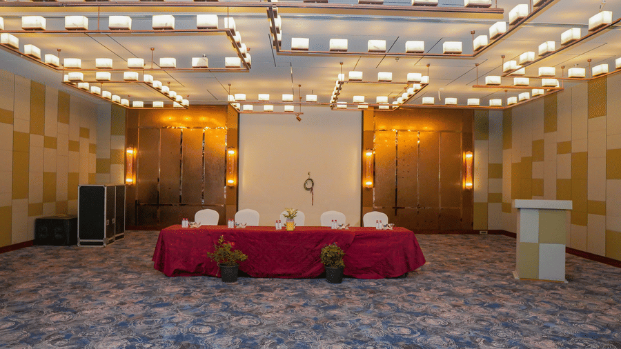 A photo of a stage area in an event room, with a table draped in a red cloth and a podium, waiting for a speaker.