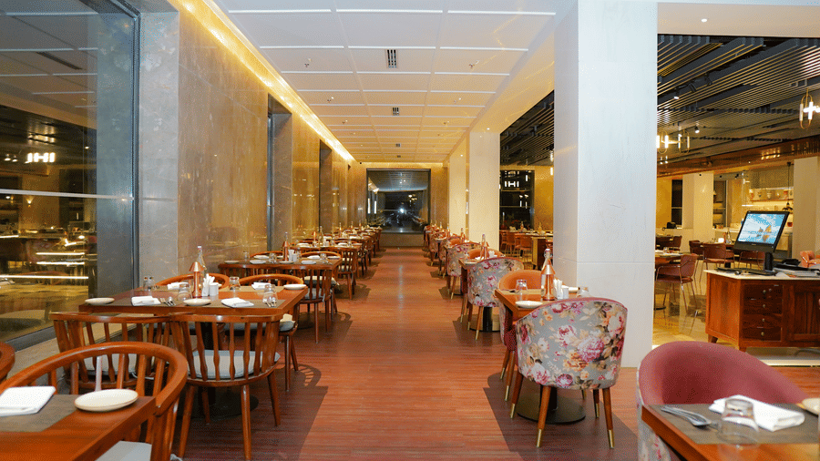 A long, well-lit indoor dining corridor with wooden and floral upholstered seating at Pushkara Resort & Spa.