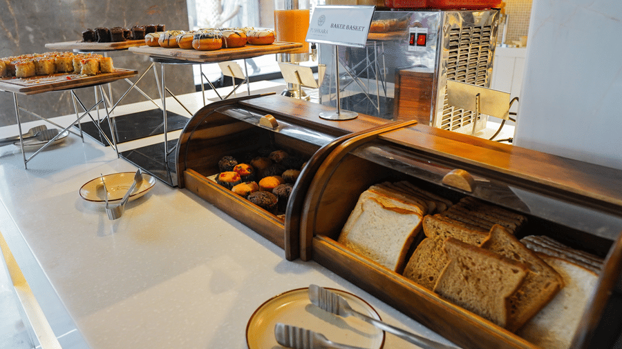 A well-stocked breakfast buffet with a wooden bread box, pastries, and juice on a white counter at Pushkara Resort & Spa.