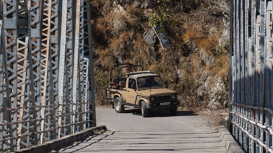 A jeep with an open back just about to pass through a suspended bridge during the day
