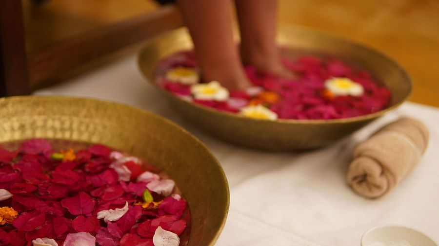 A person with their legs in a brass plate with water having rose petals