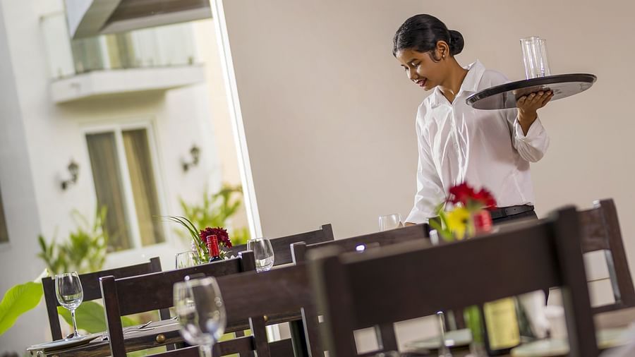 a staff member looking down while holding a tray with a glass in it - The Tanisi Hotels & Resorts, Goa
