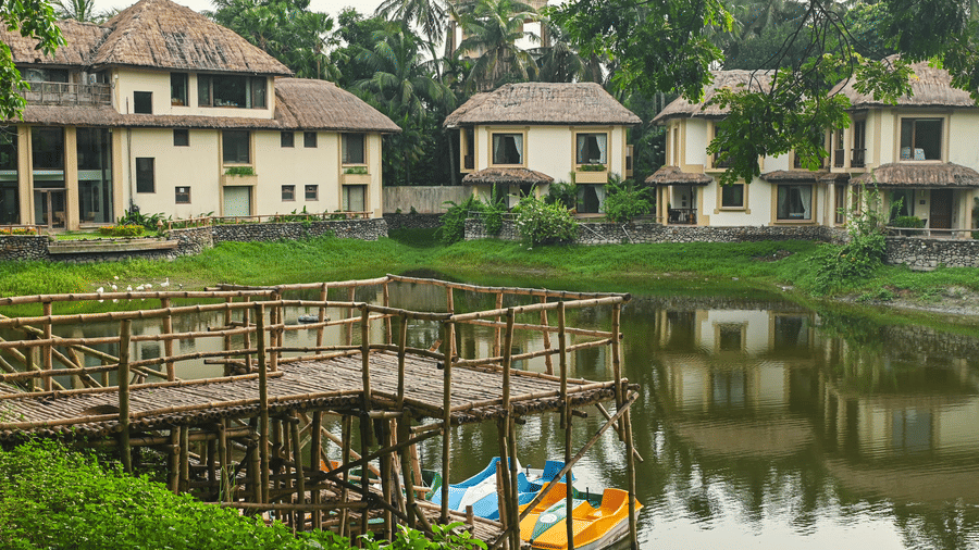  A boating area at Vedic Village with trees, plants, boats, and cottage facades.