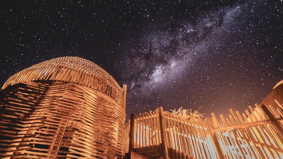 A traditional thatched bamboo hut at Evolve Back Kalahari resort under a breathtaking Milky Way starry night sky