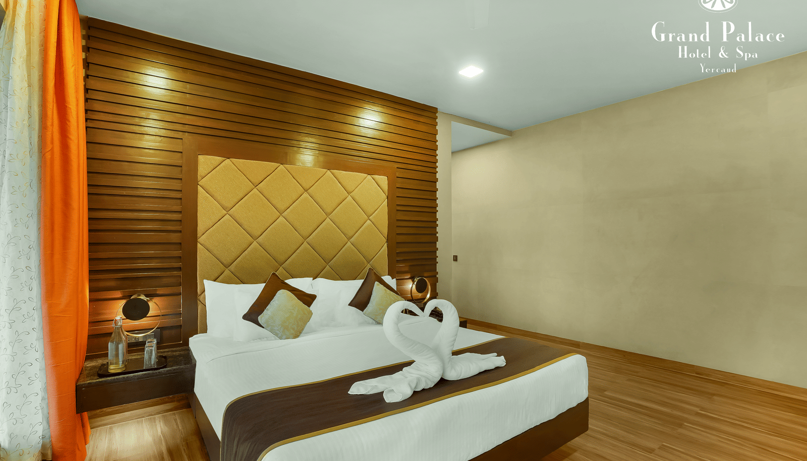 Artist Suite at Grand Palace, Yercaud with double bed, bedside tables, headboard, lighting and curtains, showing modern indoor accommodation.