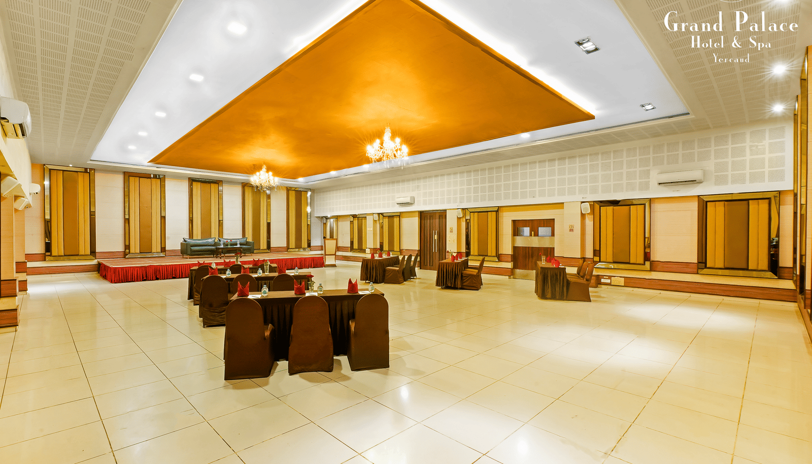 A corner view of the event space area at Grand Palace, Yercaud arranged with sofa seating, open area, chandeliers, panoramic windows, and polished flooring for gatherings.