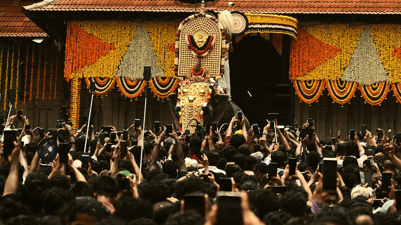 A large crowd of people gathers in front of a traditional, multi-tiered temple building during a festival.