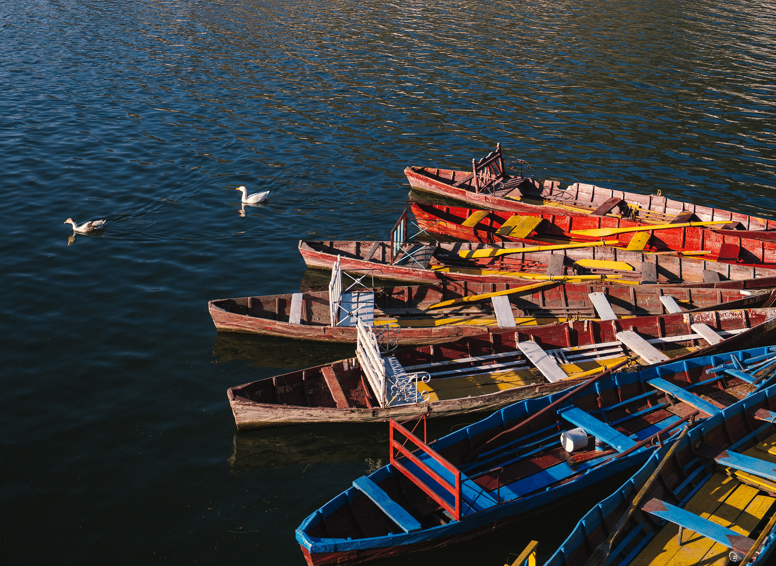 Boats are neatly arranged on a serene lake, surrounded by towering mountains.