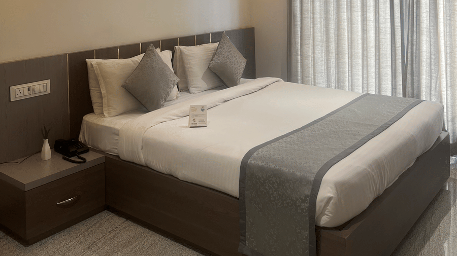 Focus on the double bed in the Deluxe Room with Road View at Daksh The Valley Resort, Saputara, seen beside long closed curtains on one side of the room.