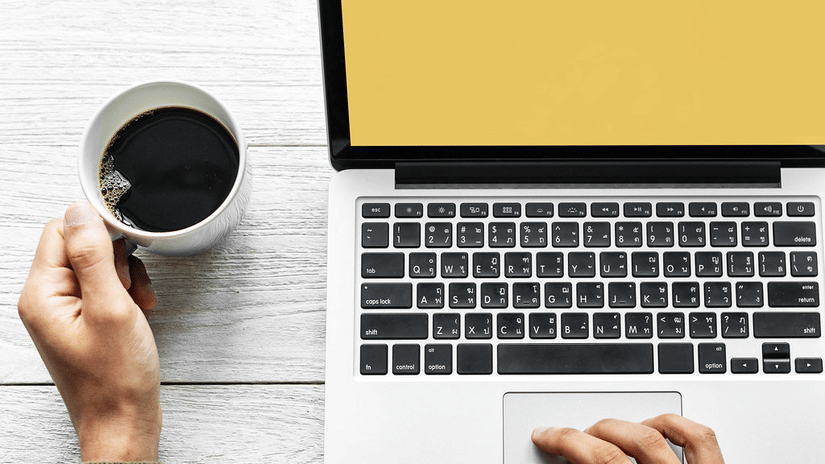 A person using a laptop while holding a cup of coffee at a desk.