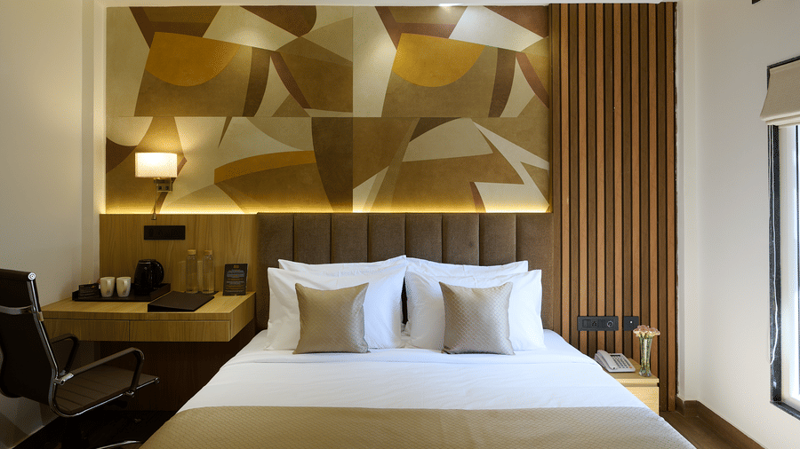 A brightly lit hotel room with a double bed, a geometric patterned accent wall behind the headboard, and a small desk area | Voyage Eastin Suites