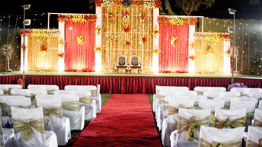 An outdoor event setup at night featuring a decorated stage with red curtains behind rows of white chairs at Garh Govind.