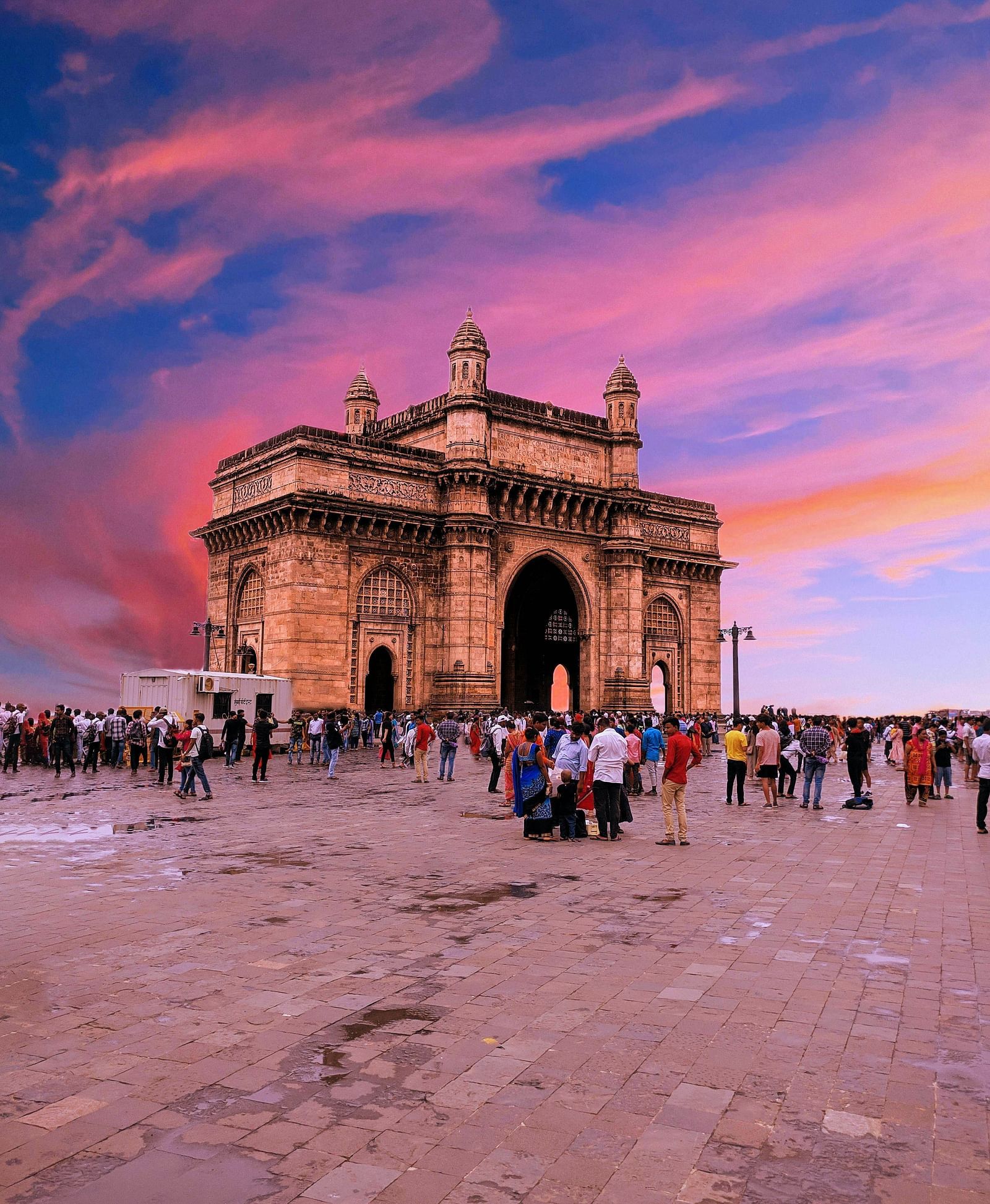 The Gateway of India lit by the warm glow of sunset with a bustling crowd in the foreground