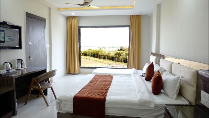 Well lit bedroom at the Aanandam Hotel Resort with a king bed,  a desk with tea maker and a window overlooking greenery.
