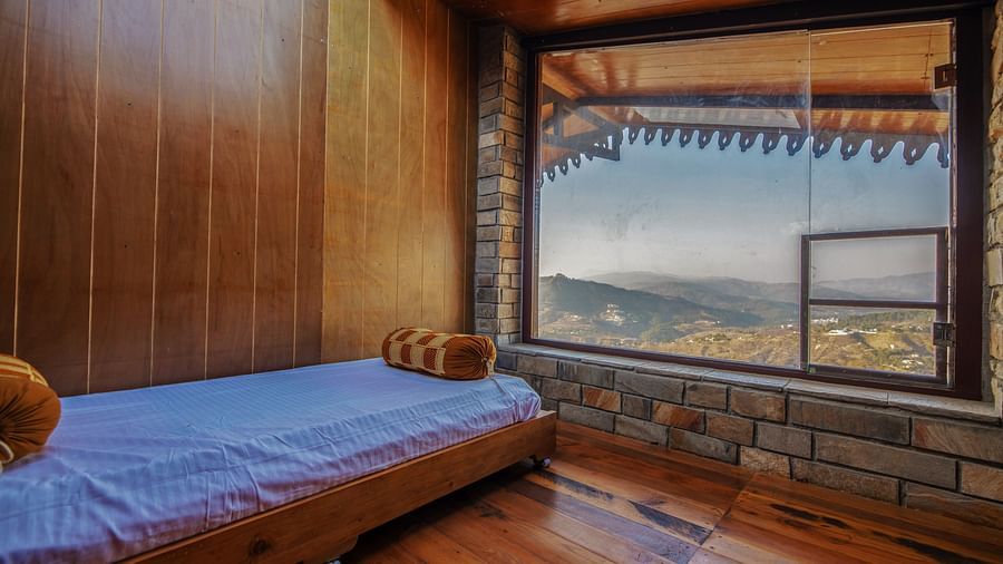 A cosy room with wooden walls, a single bed, and a large window showcasing mountain views. - Blusalzz Homes The Himalayan Bungalow, Almora