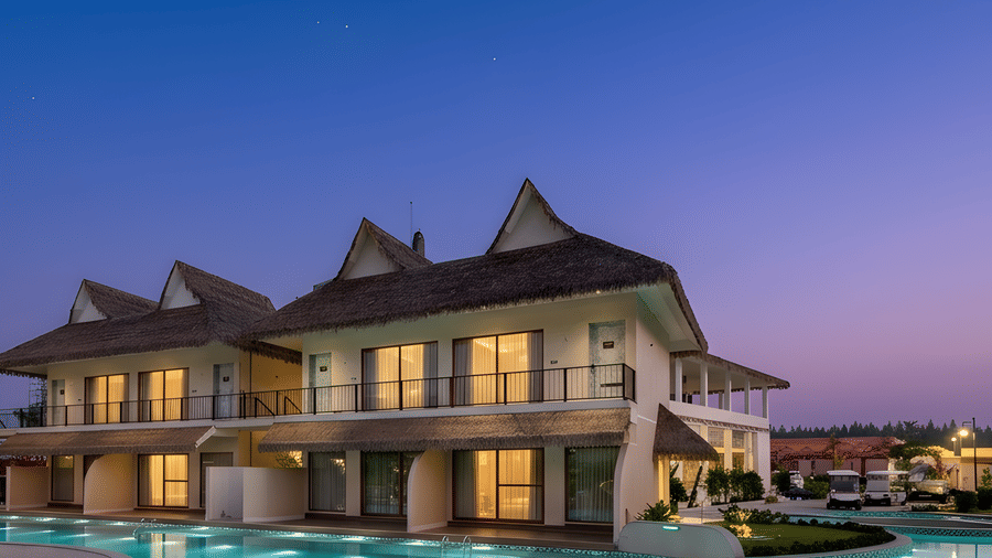 2-storey thatched-roof villas are illuminated at dusk next to a swimming pool under a purple and blue sky at Avanya Resorts N Retreat.