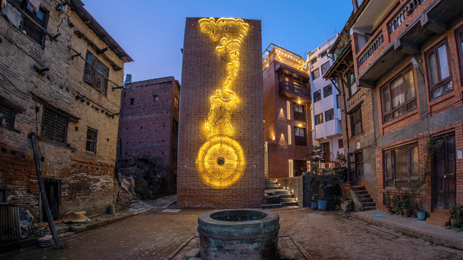 Evening street scene near The Nanee, Bhaktapur, Nepal. traditional buildings frame a large illuminated sculpture and decorative lighting.