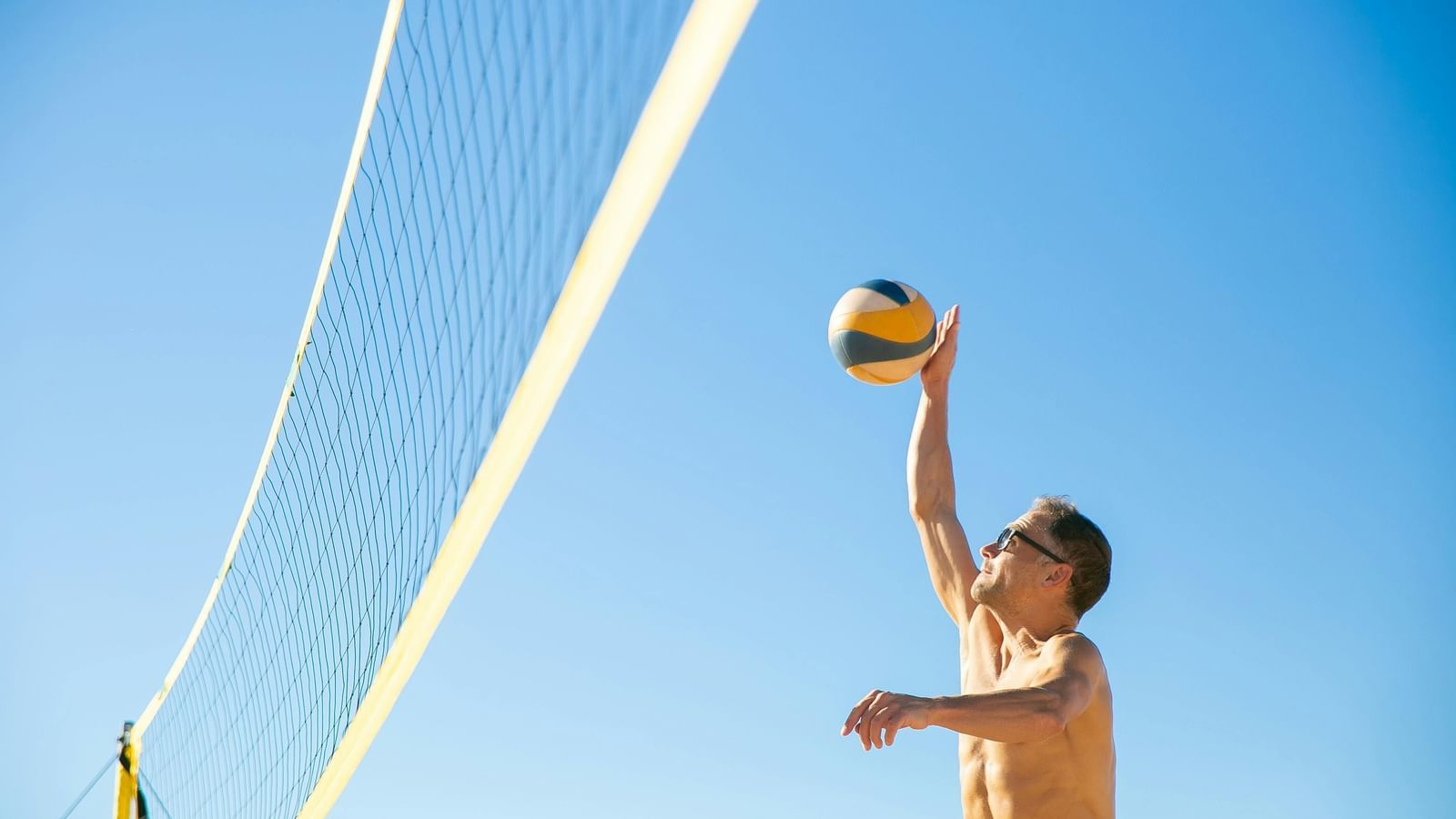 A person jumps to hit a volleyball over the net during a beach volleyball game under a clear sky.