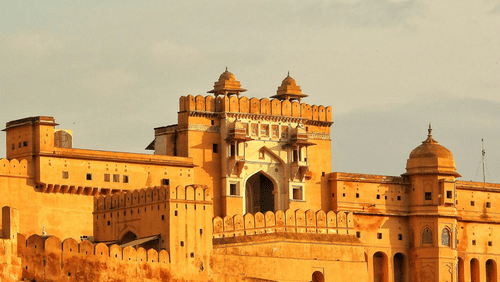 A fort with an arched entrance and domed towers stands under a light sky.