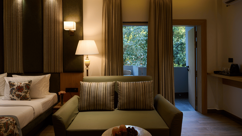 A hotel room focused on a living area with a sofa, a side table with a lamp, and drapes covering large windows leading to the outside | Voyage Eastin Suites